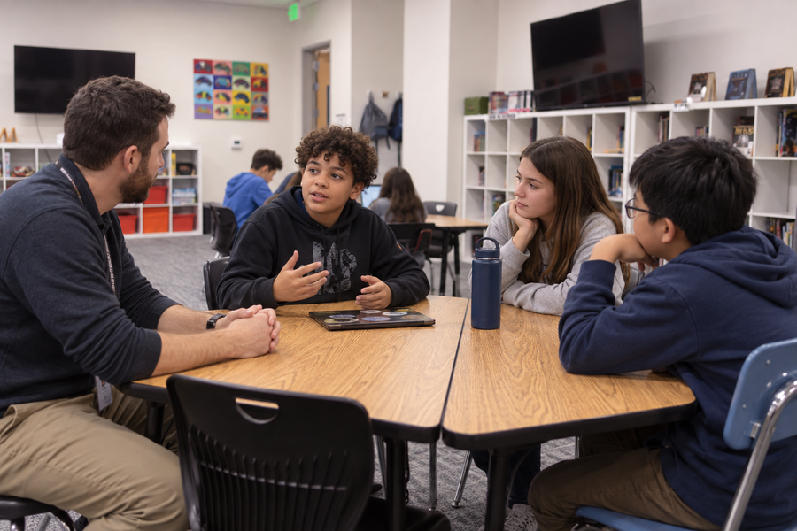 Teacher and three students discussing work around a table.