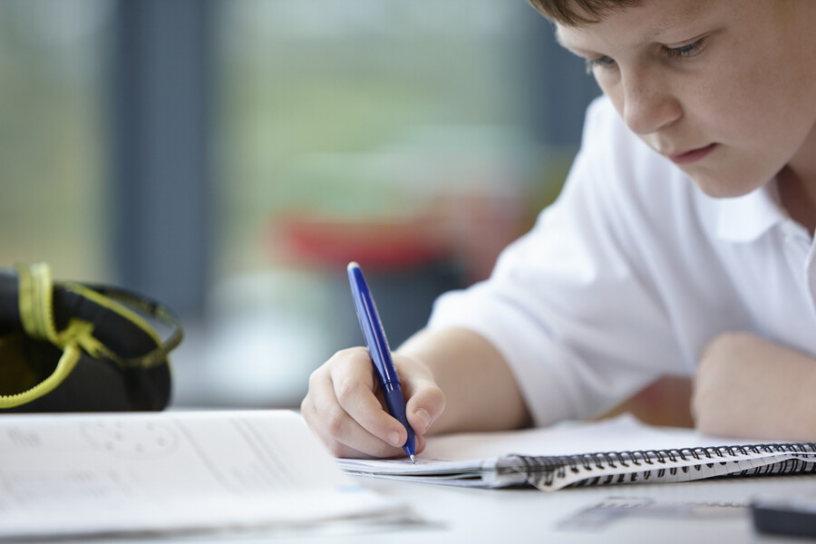 Child writing in a notebook with a pen.