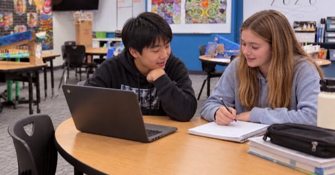 Two students working together beside a laptop and notebook. Two students working together beside a laptop and notebook.